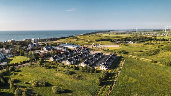 An aerial view of a coastal town with residential buildings, a marina, and wind turbines in the distance.