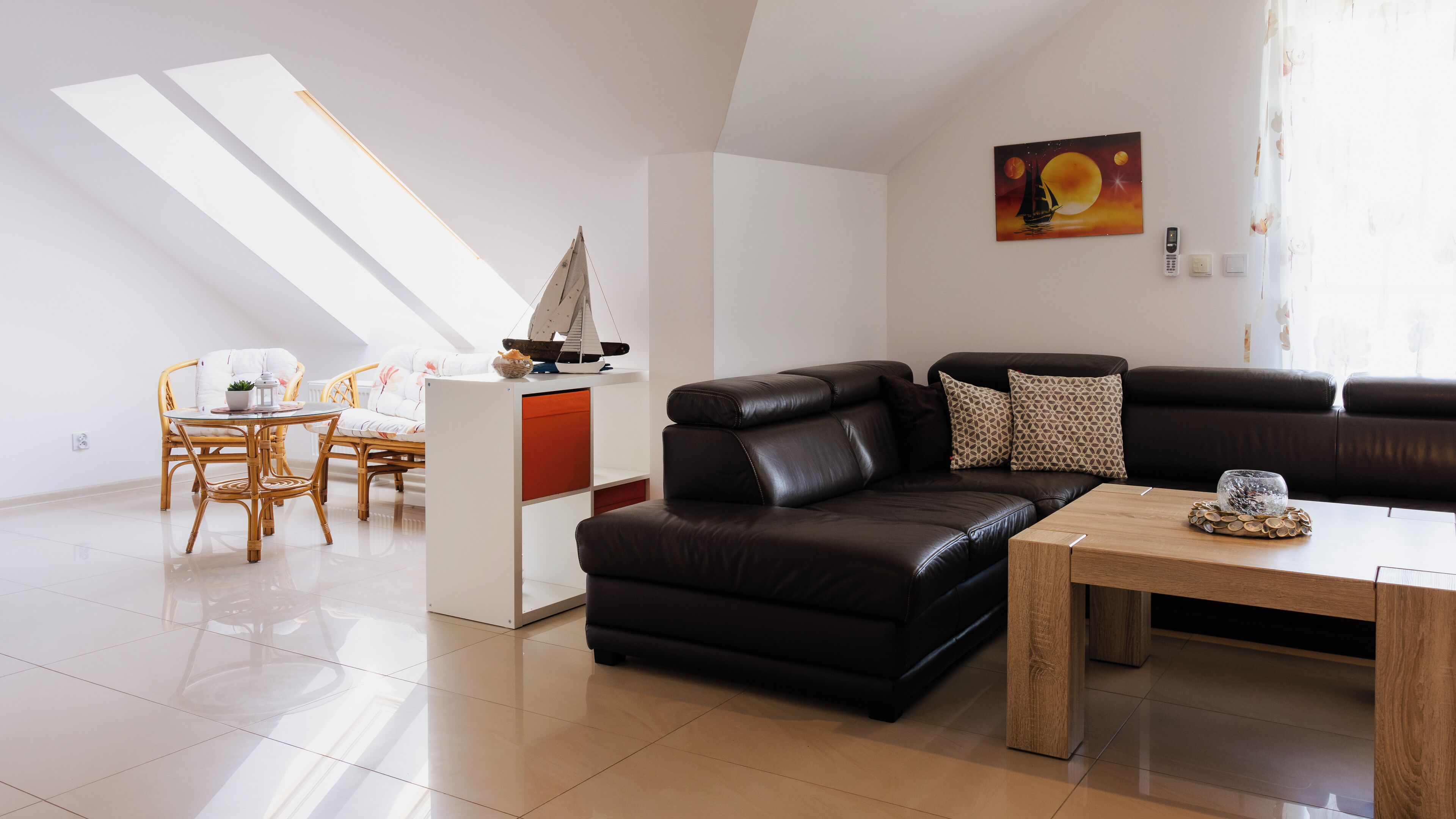Un salon moderne avec un canapé en cuir noir, une table basse en bois et un coin repas avec des chaises en osier.