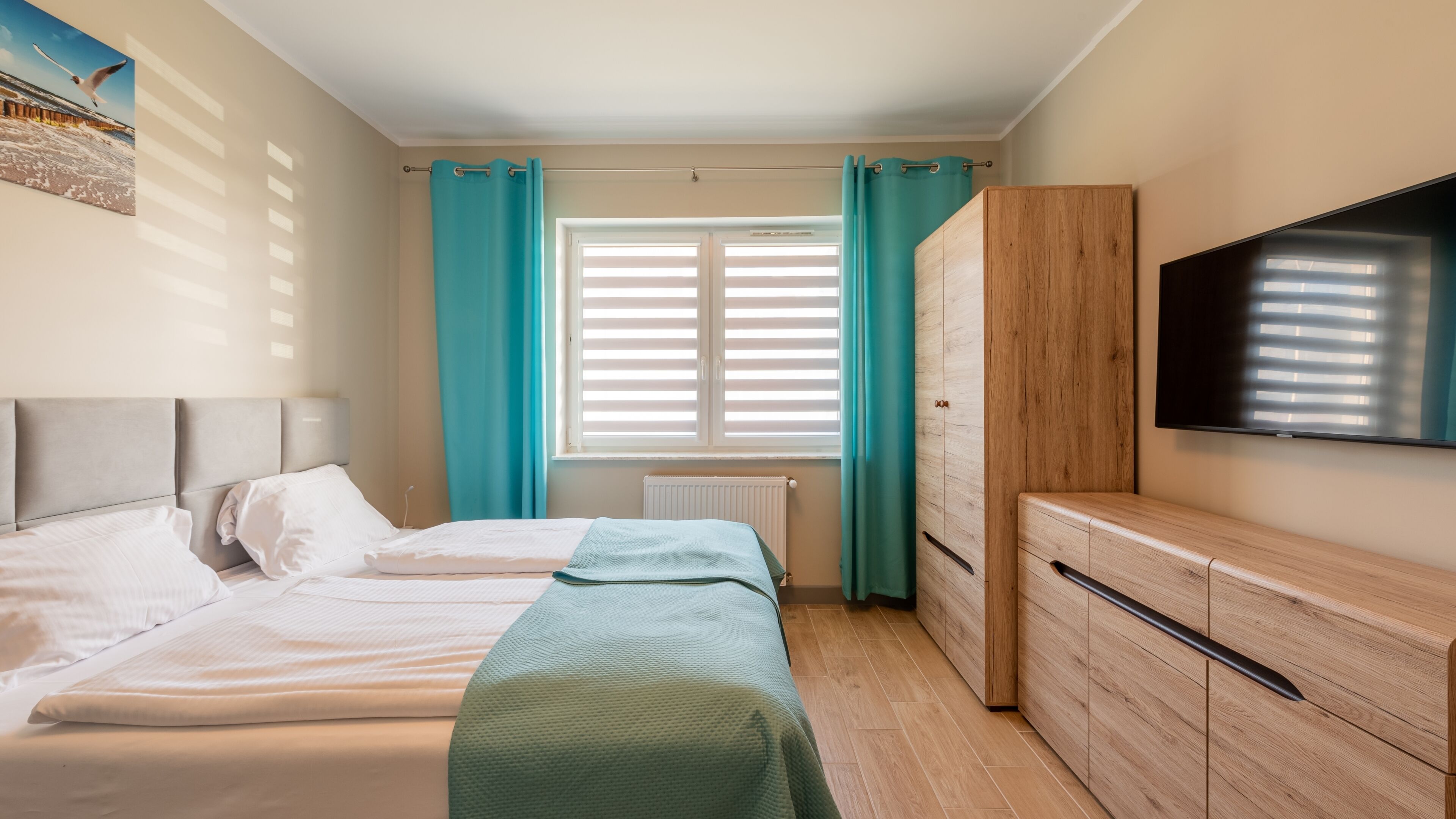 Une chambre à coucher avec un lit, une armoire en bois, un téléviseur et une fenêtre avec des rideaux.