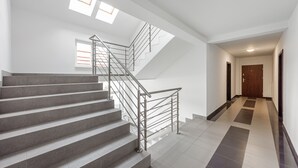 Una escalera moderna con barandillas metálicas que conduce a una plataforma, un pasillo con una puerta de madera y un piso de baldosas.