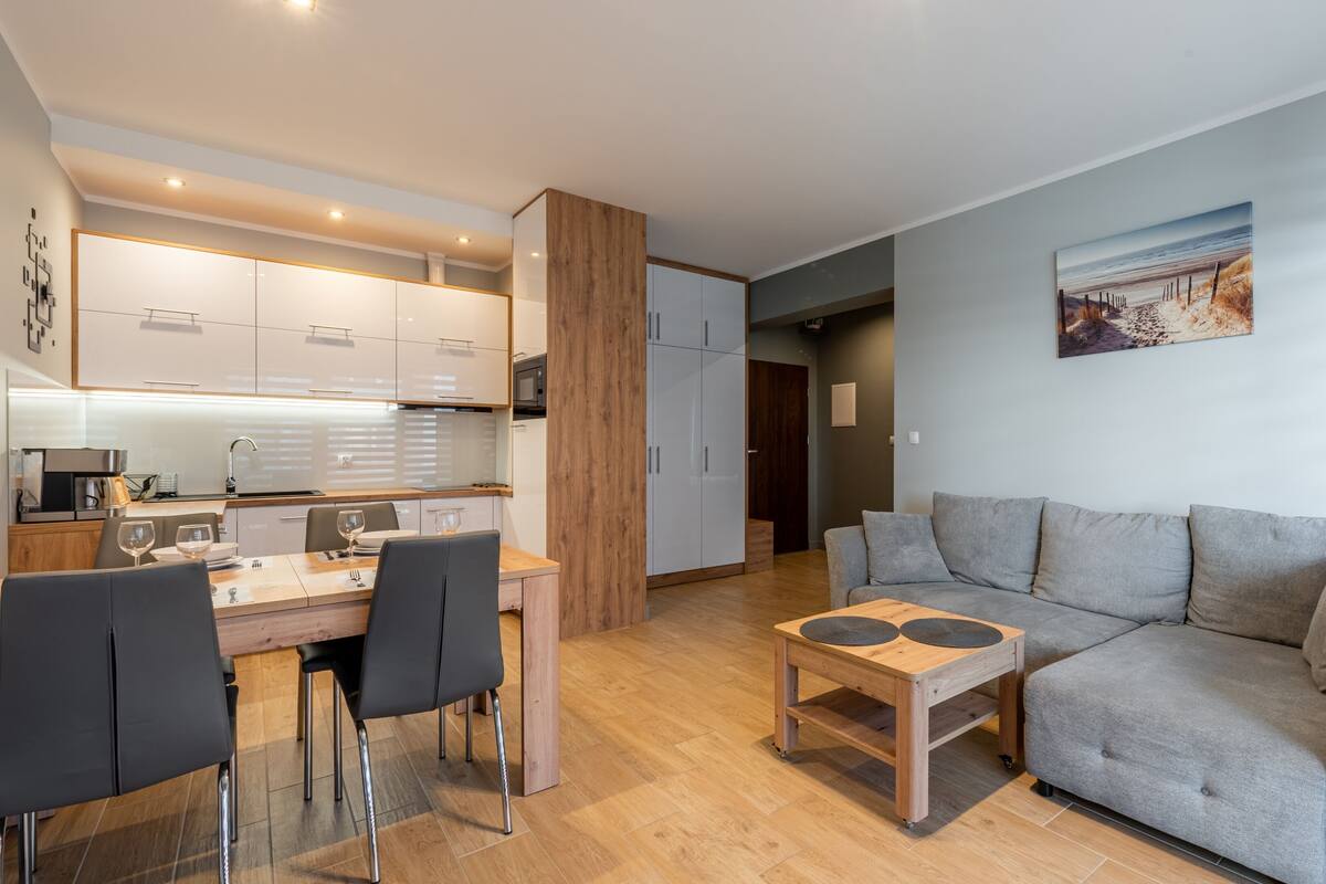 Una sala de estar moderna con un sofá gris, una mesa de centro de madera y un comedor con mesa y sillas.