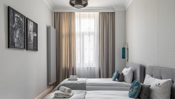 Una habitación de hotel con dos camas, un radiador, una ventana con cortinas e imágenes enmarcadas en la pared.
