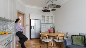 Una cocina moderna con armarios blancos, un refrigerador de acero inoxidable y un comedor con mesa y sillas de madera.