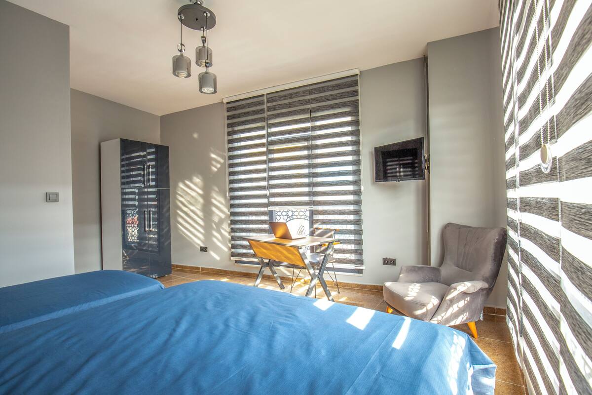 A bedroom with two beds, a desk, a chair, and a wardrobe.
