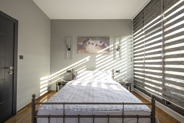 A bedroom with a bed, a painting on the wall, and a window with blinds.
