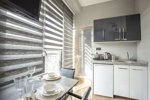 A modern kitchen with a dining area, featuring a kitchen island, a built-in oven, and a window with blinds.