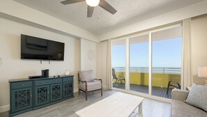 Una sala de estar con televisor, un mueble de madera, una silla, una mesa y un balcón con vistas.