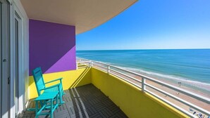 Ein Balkon mit Blick auf den Strand, eine violette Wand und ein türkisfarbener Stuhl.