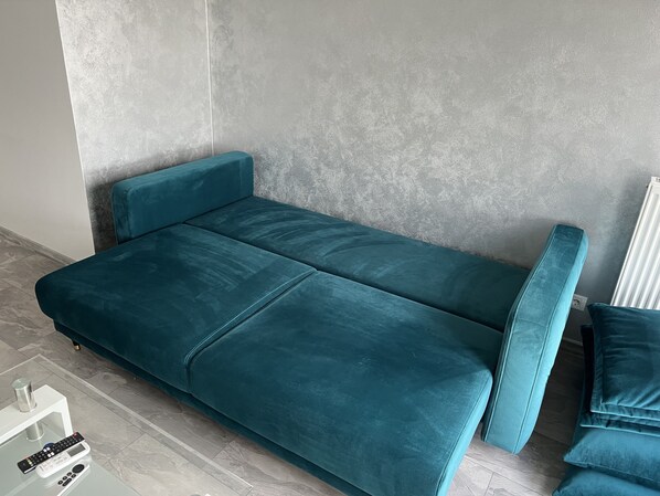 A teal sofa with a matching bench in a modern room with a concrete wall and a tiled floor.