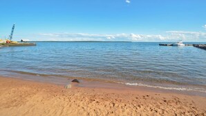 En strand med klart vatten, en båt förtöjd till höger och en kran till vänster.