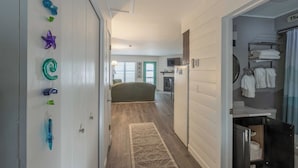 En hall som leder till ett sovrum med en säng, ett badrum med handfat och handdukar samt ett köksområde med ett kylskåp.