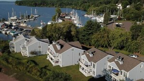 En småbåtshamn med flera förtöjda båtar, omgiven av bostadshus med balkonger och en sjö i bakgrunden.