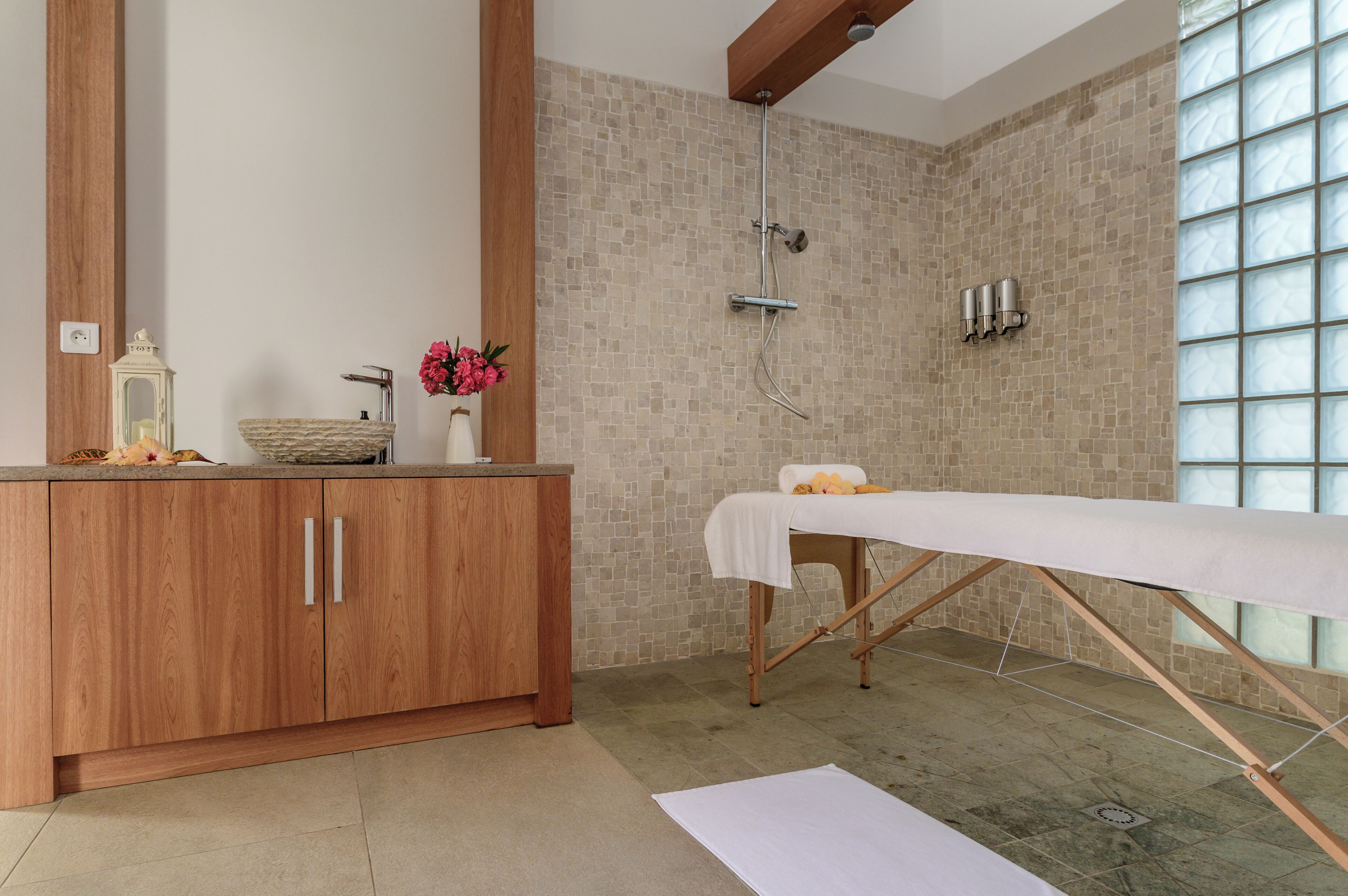A bathroom with a wooden vanity, a large mirror, a shower with a glass enclosure, and a massage table.