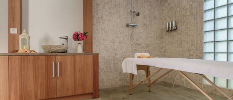 A bathroom with a wooden vanity, a large mirror, a shower with a glass enclosure, and a massage table.
