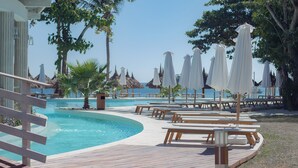 Un área junto a la piscina con terraza de madera, sillas de descanso y sombrillas.