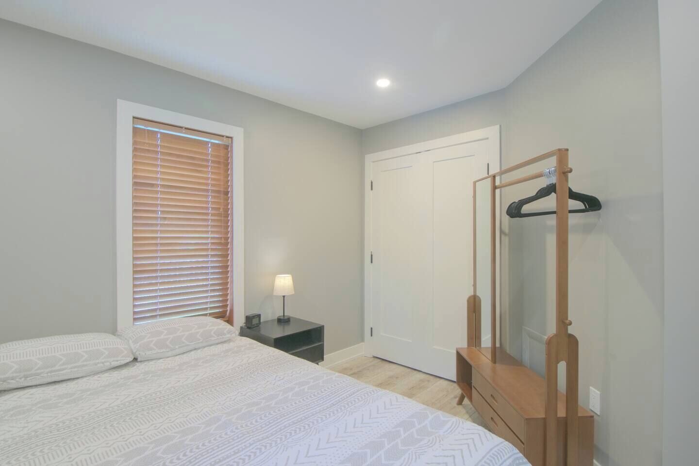 Une chambre à coucher comprenant un lit, une table de chevet avec une lampe, une commode en bois, un miroir et une armoire.