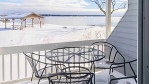 Ett takförsett utomhusområde med ett bord och stolar, med utsikt över ett snötäckt landskap och en sjö eller ett annat vattendrag.