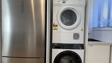 Une cuisine compacte dotée d’un réfrigérateur en acier inoxydable et d’un appareil combiné lave-linge et sèche-linge intégré.