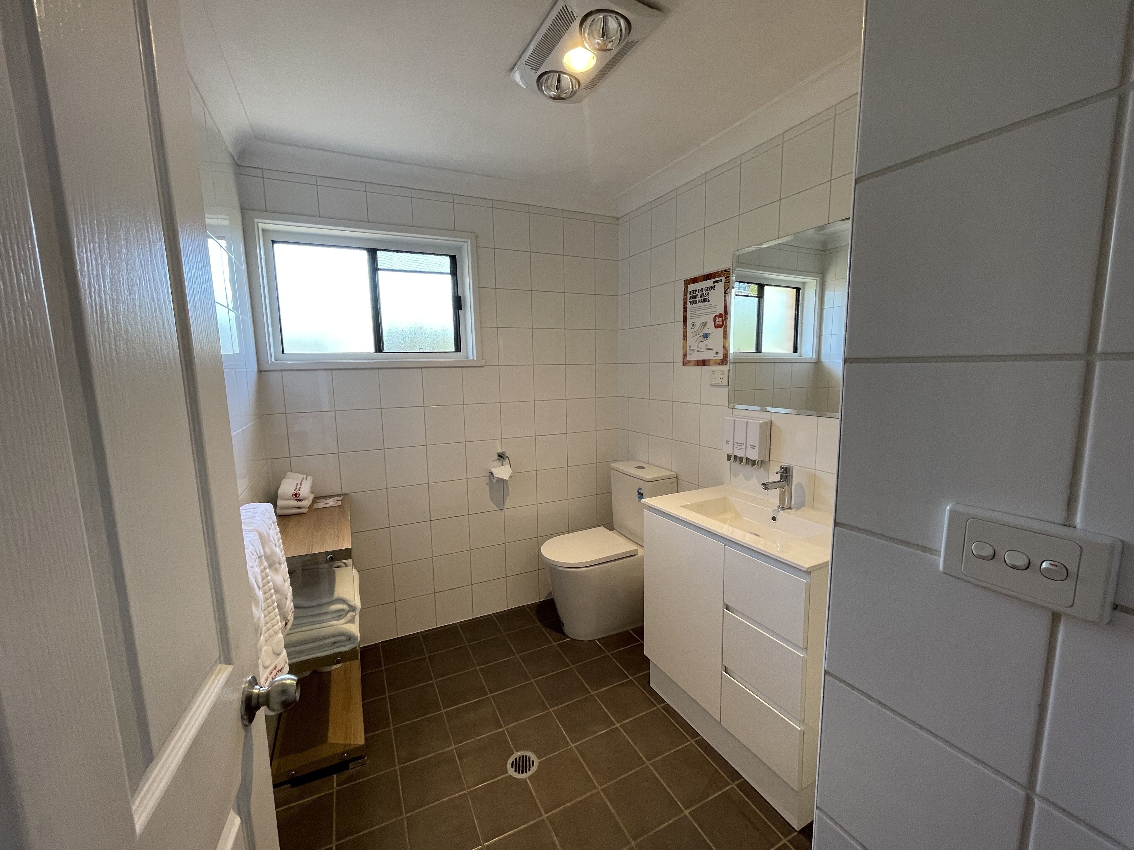 A bathroom with white tiles, a toilet, a sink, and a window.