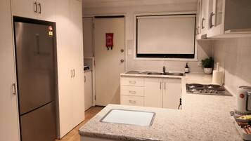 A modern kitchen with white cabinets, a stainless steel refrigerator, a double sink, and a gas stove.