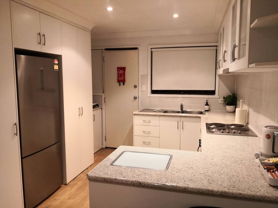 A modern kitchen with white cabinets, a stainless steel refrigerator, a double sink, and a gas stove.