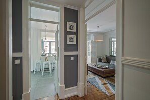 A hallway leading to a dining area with a table and chairs, a living room with a sofa and a rug, and artwork on the walls.