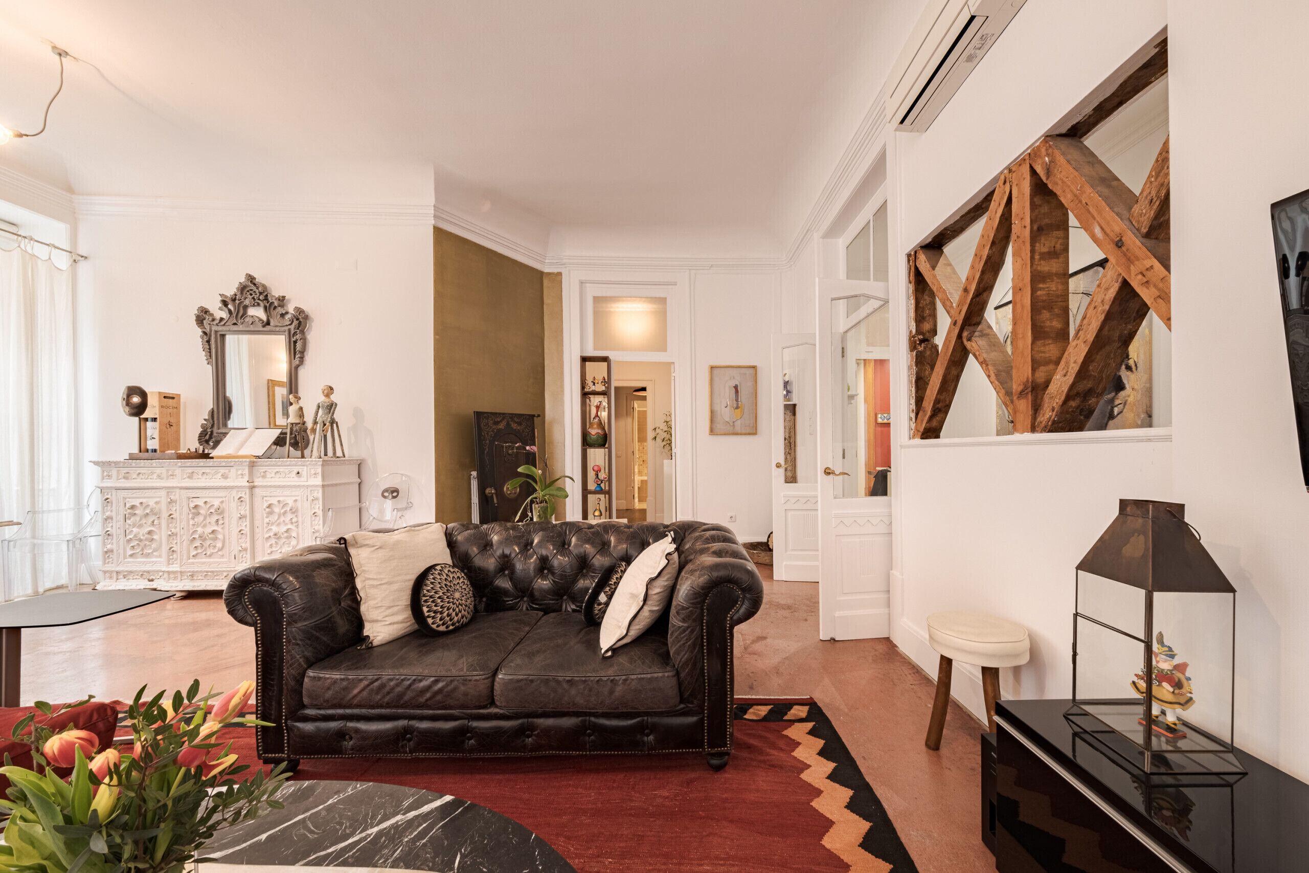 A living room with a dark leather sofa, a white cabinet, and a large mirror.