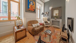 A living room with a brown sofa, a patterned rug, a wooden coffee table, a white armchair, a fireplace, and a large window. - Central Apartment 2BR/2BA | Balcony | Lift in Baixa (Lisboa ciudad)
