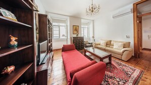 A living room with a sofa, a coffee table, a red sofa, a bookshelf, and a chandelier. - Family Friendly 3BR/2BA Central Apartment in Baixa (Lisboa ciudad)