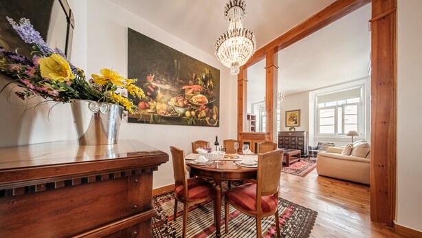 A dining area with a wooden table set for four, surrounded by chairs. A chandelier hangs from the ceiling, and a large painting adorns the wall. - Family Friendly 3BR/2BA Central Apartment in Baixa (Lisboa ciudad)