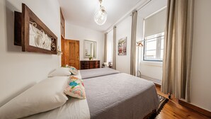 A bedroom with two beds, a wooden wardrobe, a mirror, and a window with curtains. - Family Friendly 3BR/2BA Central Apartment in Baixa (Lisboa ciudad)