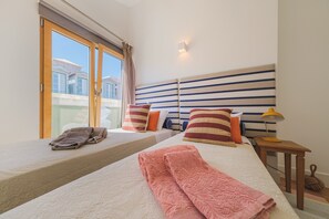 Une chambre d’hôtel avec deux lits, une tête de lit à rayures et une vue sur les bâtiments, visible à travers une porte coulissante.