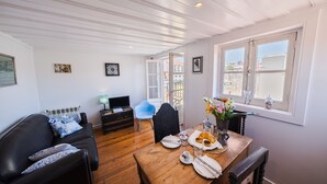 Ein Zimmer mit einem Holzespeisetisch, der für ein Frühstück gedeckt ist, einer schwarzen Ledersofa, einem blauen Stuhl und einem Fernseher auf einem Schrank.
