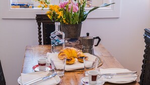 Ein Holztisch, gedeckt für ein Frühstück, mit Croissants, einer Flasche, einer Kaffeekanne und einer Blumenvase.