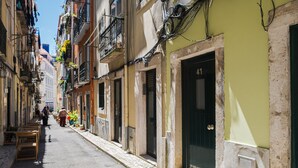 Eine schmale Straße, gesäumt von Gebäuden, einige davon mit Balkonen und Außenbestuhlung.
