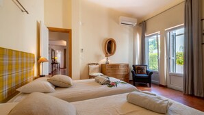 A hotel room with two beds, a wooden dresser, a chair, a mirror, and a window with curtains.