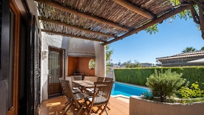 An outdoor patio with a table and chairs, a pool, and a view of the surrounding area.