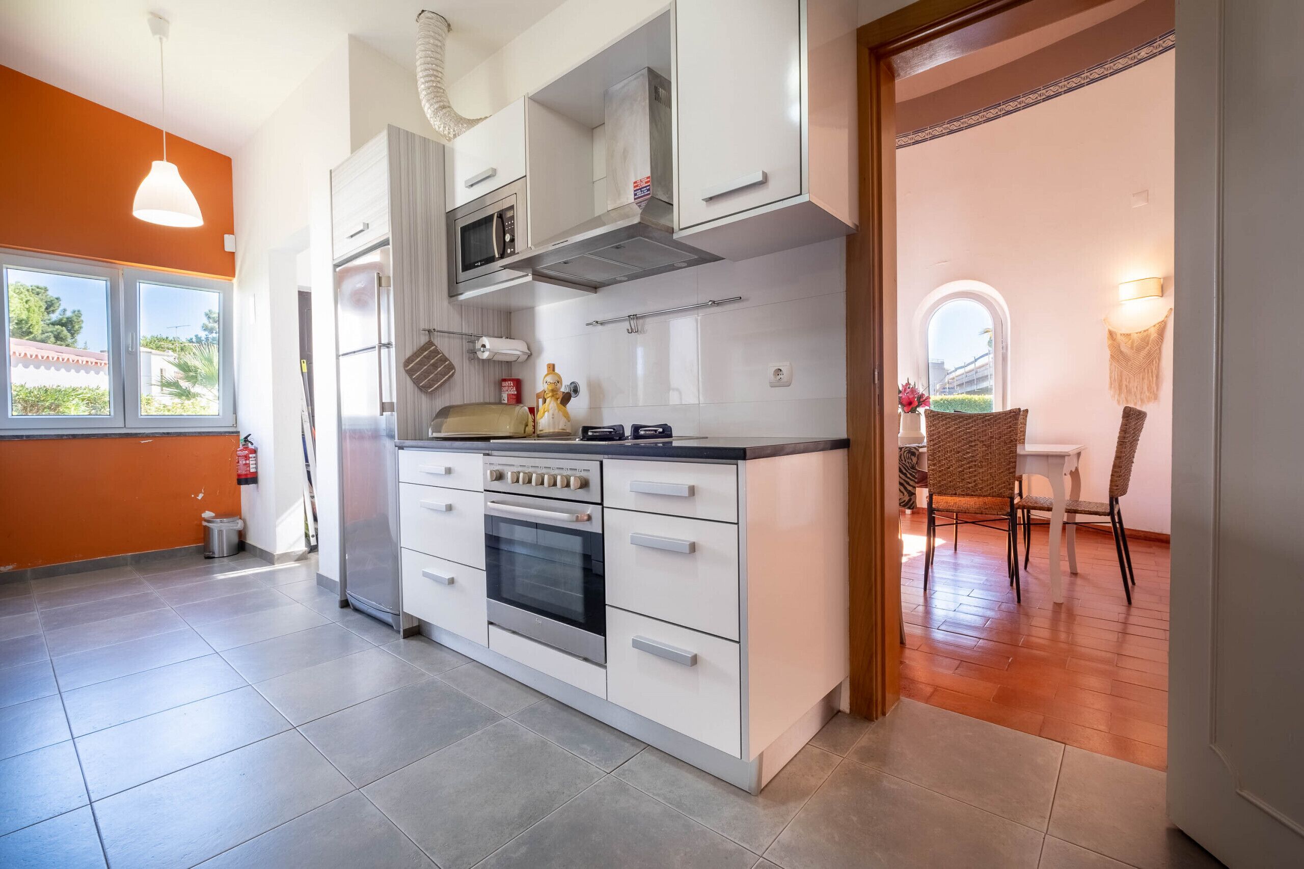 A modern kitchen with white cabinets, a built-in oven, and a microwave. There is a window providing natural light and a view of the outdoors.