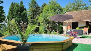 A backyard with a swimming pool, a covered patio area, and a wooden deck.