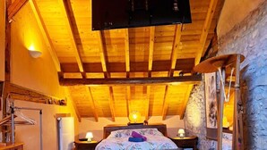 A bedroom with a wooden ceiling, a bed, a dresser, and a stone wall.