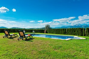 En pool med två solstolar och ett litet bord, omgiven av en välskött gräsmatta och en häck.