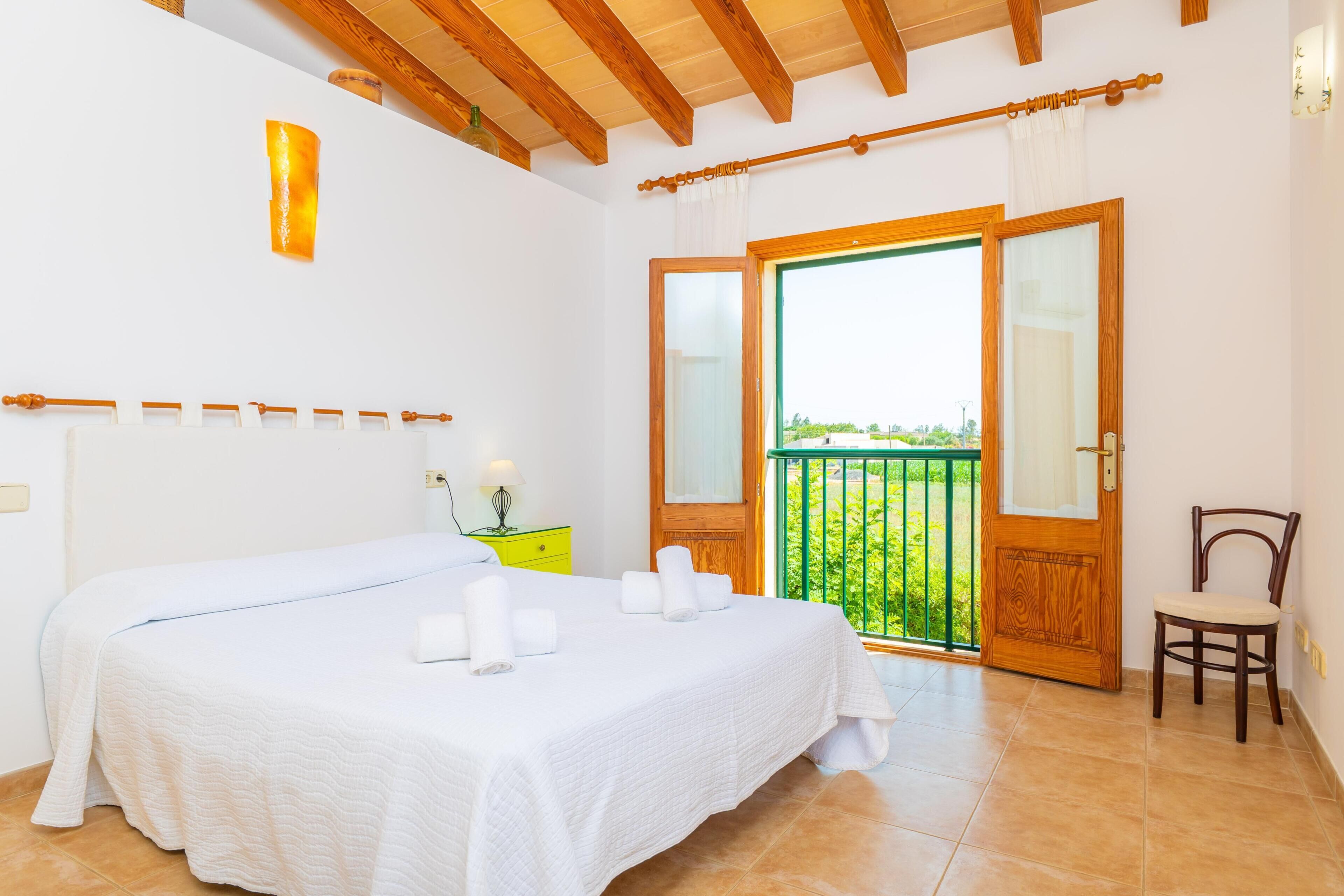 Une chambre à coucher avec un lit, une chaise, une table de chevet, une fenêtre et un balcon.