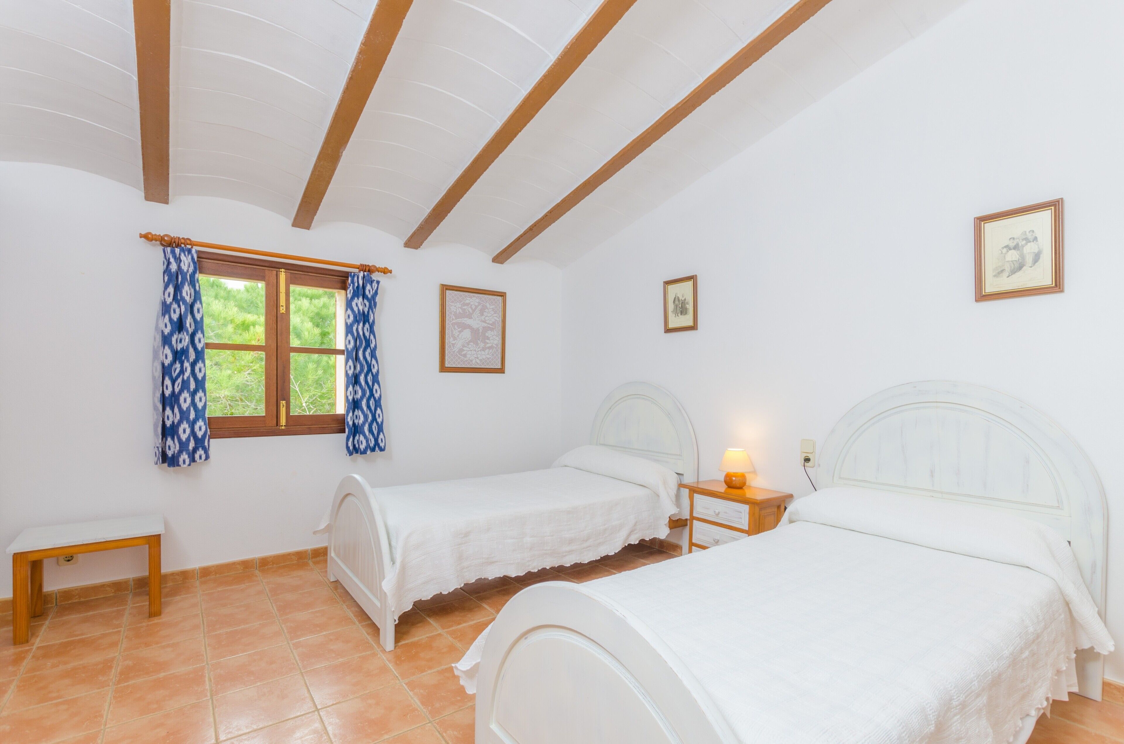 Een slaapkamer met twee eenpersoonsbedden, een bankje en een raam met gordijnen met patroon.