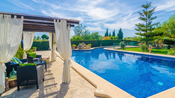 A swimming pool with a pergola and seating area, surrounded by greenery and a clear sky. - ES CAMP FRED -  beautiful villa with spectacular private pool and impressive garden. Free (Felanitx)
