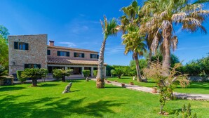 A stone building with a tiled roof, surrounded by a well-maintained garden with palm trees and various shrubs. - ES CAMP FRED -  beautiful villa with spectacular private pool and impressive garden. Free (Felanitx)