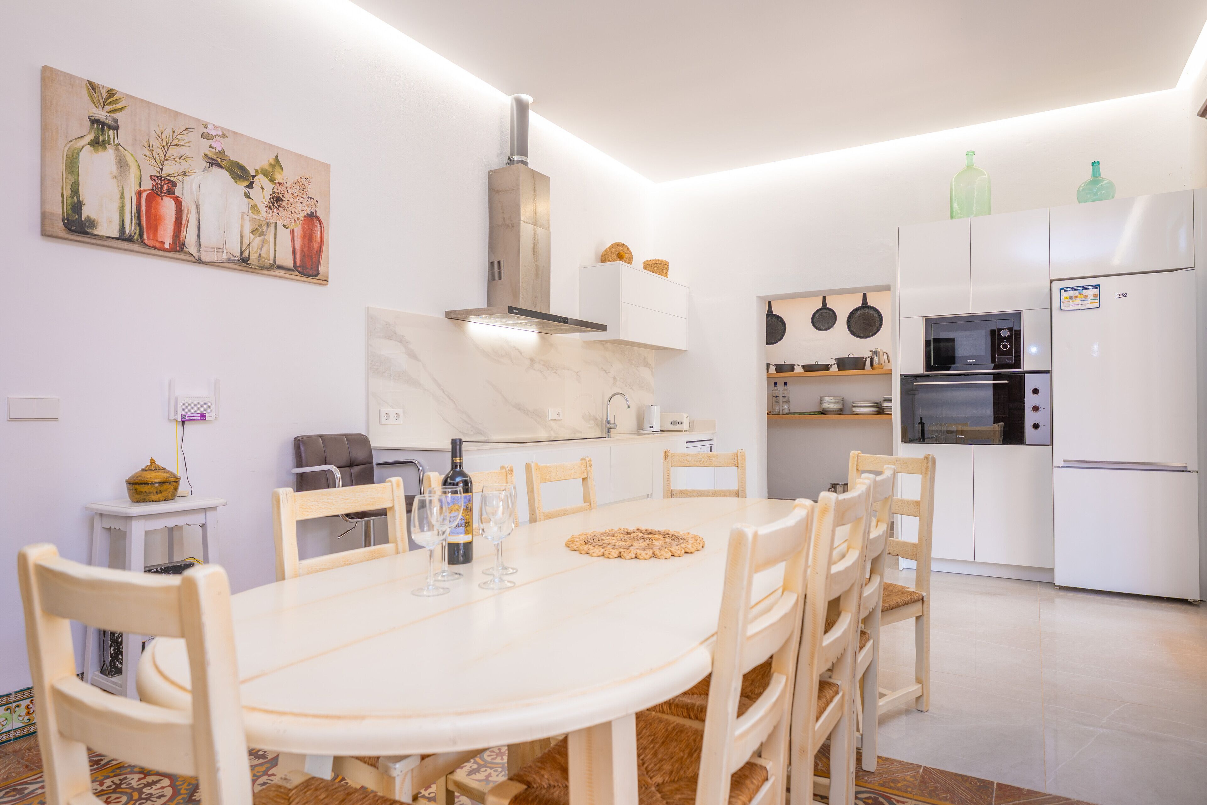 Une cuisine moderne avec des meubles blancs, une table à manger avec des chaises et un tableau accroché au mur.