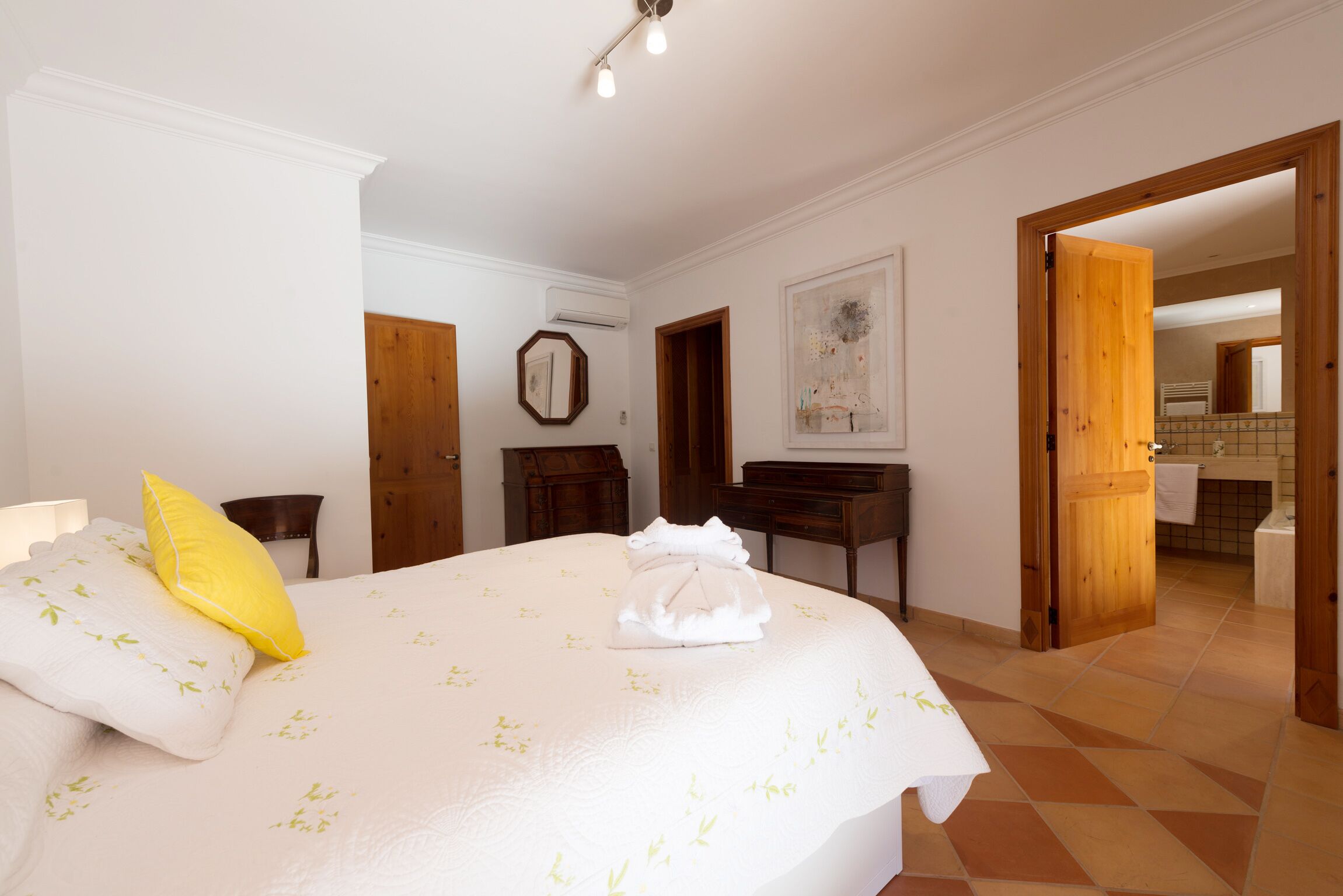 A hotel room with a bed, a wooden desk, a mirror, and a bathroom visible through an open door.