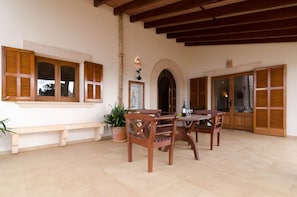 Un patio con mesa y sillas de madera, un banco y contraventanas de madera en las ventanas.