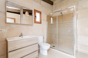 Une salle de bain avec un meuble-lavabo en bois, des toilettes blanches et une cabine de douche en verre.