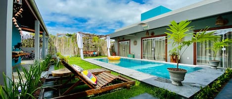 A modern outdoor pool area with a wooden deck, lounge chairs, and a small garden with potted plants.